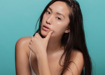 Attractive young asian woman with glowing skin. Korean female with beautiful skin looking at camera against blue background.