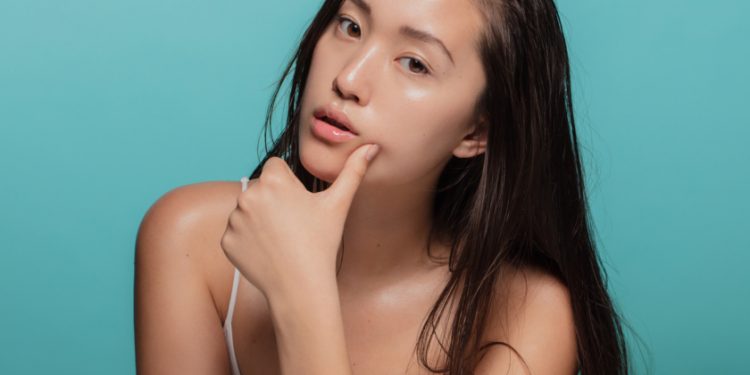 Attractive young asian woman with glowing skin. Korean female with beautiful skin looking at camera against blue background.