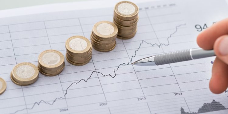 Cropped image of businessman's hand with pen analyzing line and coins graphs on desk